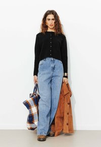 Cardigan noir à côtes, jean taille haute bleu clair, manteau en suede marron, sac fourre-tout à carreaux et chaussures imprimé léopard.