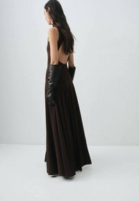 Braunes rückenfreies Maxikleid mit plissiertem Rock und Schulterträgern, kombiniert mit langen schwarzen Lederhandschuhen, die eine glatte Textur zeigen.
