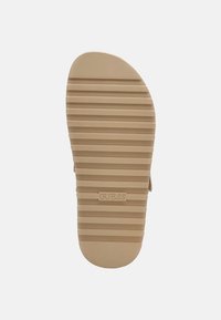 Tan rubberen zool met horizontale groeven en een ronde neus. Kenmerkt de ingebedde merknaam "GUESS" nabij de hak.