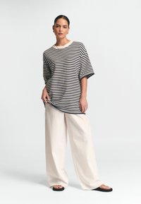 Röstripeeritud T-särk laiade varrukatega, tumesinine ja kreemjas; kombineeritud vabade neutraalsetes värvitoonides pükstega ja lapikute mustade sandaalidega, minimaalne disain.