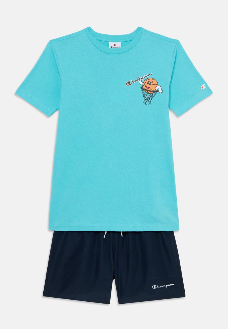 Tirkīza kokvilnas T-krekls ar mazu grafiku, kurā attēlots basketbols un spēlētājs, kombinēts ar tumši ziliem šortiem, kur viens no kājstarpes ir balts logo.