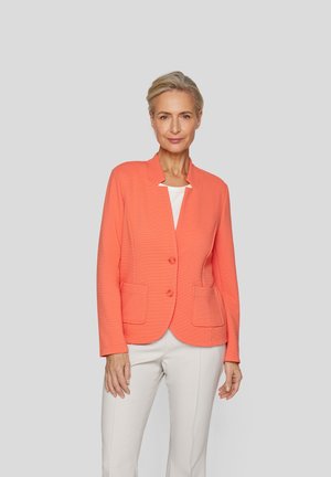 Coral blazer with a structured collar, two front pockets, and two buttons. Worn over a white top, paired with light trousers.