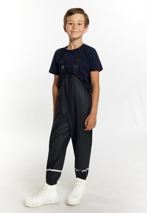 Sorte vandtætte overalls med justerbare stropper og elastiske manchetter, båret over en marineblå t-shirt, parret med hvide høj-top sneakers.