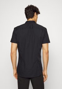 Schwarzes kurzärmliges Hemd mit geradem Saum, Punktkragen und glatter Stoffoberfläche. Einfaches Design, keine sichtbaren Muster oder Beschläge. Rückansicht gezeigt.