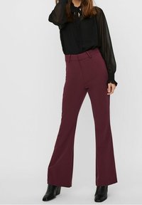 Bordeaux flared trousers met een hoge taille, gemaakt van een gladde stof. Gecombineerd met een zwarte blouse met lange mouwen en zwarte enkellaarsjes.