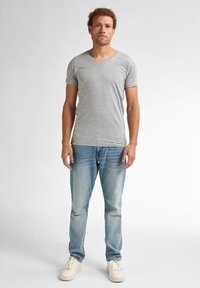Tricou gri cu mânecă scurtă și guler în V, fabricat din bumbac, asortat cu blugi de spălare medie și adidași albi. Poză de sine stătătoare pe un fundal neutru.