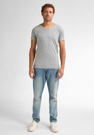 Grijze korte mouwen V-hals T-shirt gemaakt van katoen, gecombineerd met middelblauwe jeans en witte sneakers. Staande pose tegen een neutrale achtergrond.