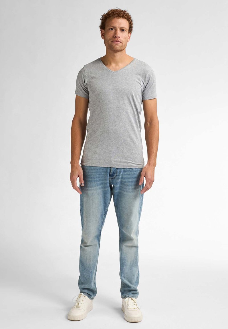Tricou gri cu mânecă scurtă și guler în V, fabricat din bumbac, asortat cu blugi de spălare medie și adidași albi. Poză de sine stătătoare pe un fundal neutru.