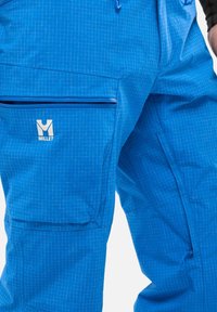 Blaue Außenhosen aus synthetischem Material, mit einem Karomuster, mehreren Taschen und einer seitlichen Tasche mit Reißverschluss. Markenlogo sichtbar.