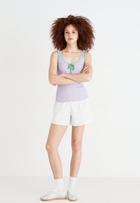 Lys lilla ribbet tank topp med grønne detaljer og en foran knute, sammen med hvite broderte kortbukser og mintgrønne sneakers.