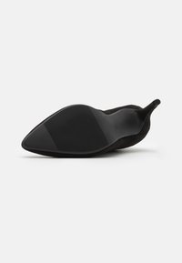 Zapato de tacón alto negro de punta afilada con parte superior de ante suave, suela de goma texturizada y un diseño elegante y aerodinámico.