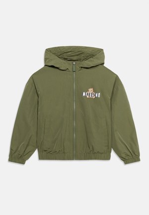 Olive green lightweight jacket with a zip front, hood, elastic cuffs, and a teddy bear logo on the chest. Smooth texture, casual design.