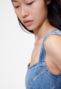 Denim bodi s širokim naramenicama, svijetloplave boje, strukturiranog dizajna i vidljivih detalja šavova, prikazujući oblik siluete prilagođene tijelu.