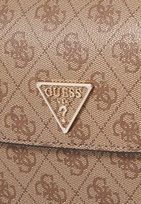 Ruskea synteettinen käsilaukku, jossa on teksturoitu pinta, ja joka sisältää näyttävän kolmiomaisen kultalevyn sekä ristiin menevän kuviolaatan.