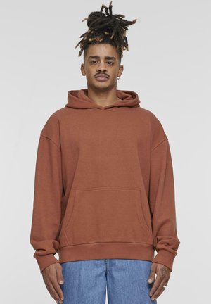 Brown hooded sweatshirt with a front pocket, loose fit, and long sleeves, paired with light blue jeans. Smooth texture, casual design.
