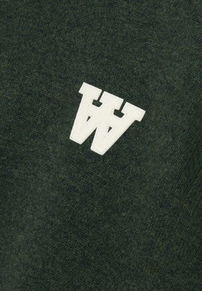 Tumma vihreä neulekangas, jossa on pehmeä rakenne; vasemmassa yläkulmassa on valkoinen, kohotettu, kaksinkertainen 'W' -logo ommeltuna.