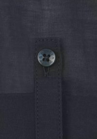 Marineblauwe stof met een gestructureerde afwerking heeft een ronde zwarte knop en een gestikte tab, wat een strakke, minimalistische uitstraling benadrukt.