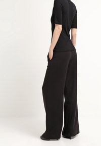 Zwarte aansluitende top met korte mouwen, gecombineerd met brede zwarte broek, die een soepele textuur en een relaxte silhouet toont. Zakken zijn zichtbaar.