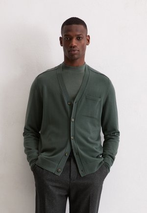 Groene cardigan met een V-hals, knoopsluiting aan de voorkant en één borstzak. Gemaakt van een zachte stof, met ribgegeven mouwen en onderkant.
