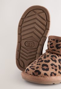 Papuc maro cu imprimeu leopard, cu partea superioară din piele întoarsă moale, vârf rotunjit și talpă din cauciuc texturată cu model zigzag pentru tracțiune.