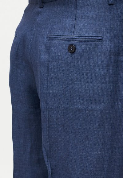 Κοντινό πλάνο σε μπλε υφασμάτινο παντελόνι ανδρών που δείχνει πίσω τσέπη με ένα μόνο μαύρο κουμπί και θηλιές για ζώνη.