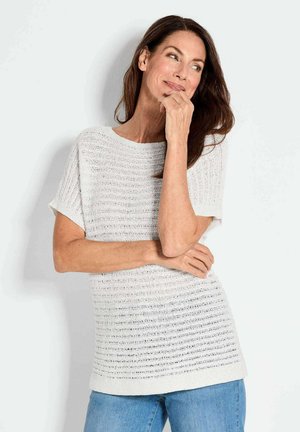 Weißes, gestricktes Kurzarmoberteil mit strukturiertem Muster und rundem Ausschnitt, kombiniert mit hellblauen Jeans.