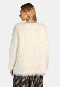 Suéter blanco esponjoso de gran tamaño con una textura suave y un detalle de collar con cuentas. Las costuras visibles y las mangas largas complementan el ajuste relajado.