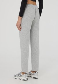 Pantaloni felpati grigi con vestibilità comoda, vita elastica e tasche laterali, abbinati a sneaker grigie e argento.