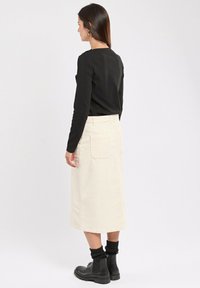 Un haut noir à manches longues associé à une jupe midi en velours côtelé crème. La jupe présente deux poches arrière et une silhouette droite. Des bottes noires complètent le look.