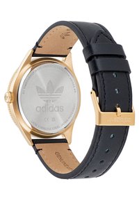 Montre en acier inoxydable doré avec logo Adidas, bracelet en cuir noir et finitions dorées. Le bracelet possède des coutures légères et des perforations.