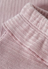 Teksturowana różowa tkanina z wzorem w zygzak, z założonym kołnierzykiem i miękkim, tkanym wykończeniem. Zbliżenie uwydatnia szczegóły.