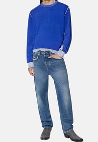 Blå crew-neck sweatshirt med kontrasterande ärmkanter, parat med blekta blå denimjeans och grå texturerade ankelstövlar.