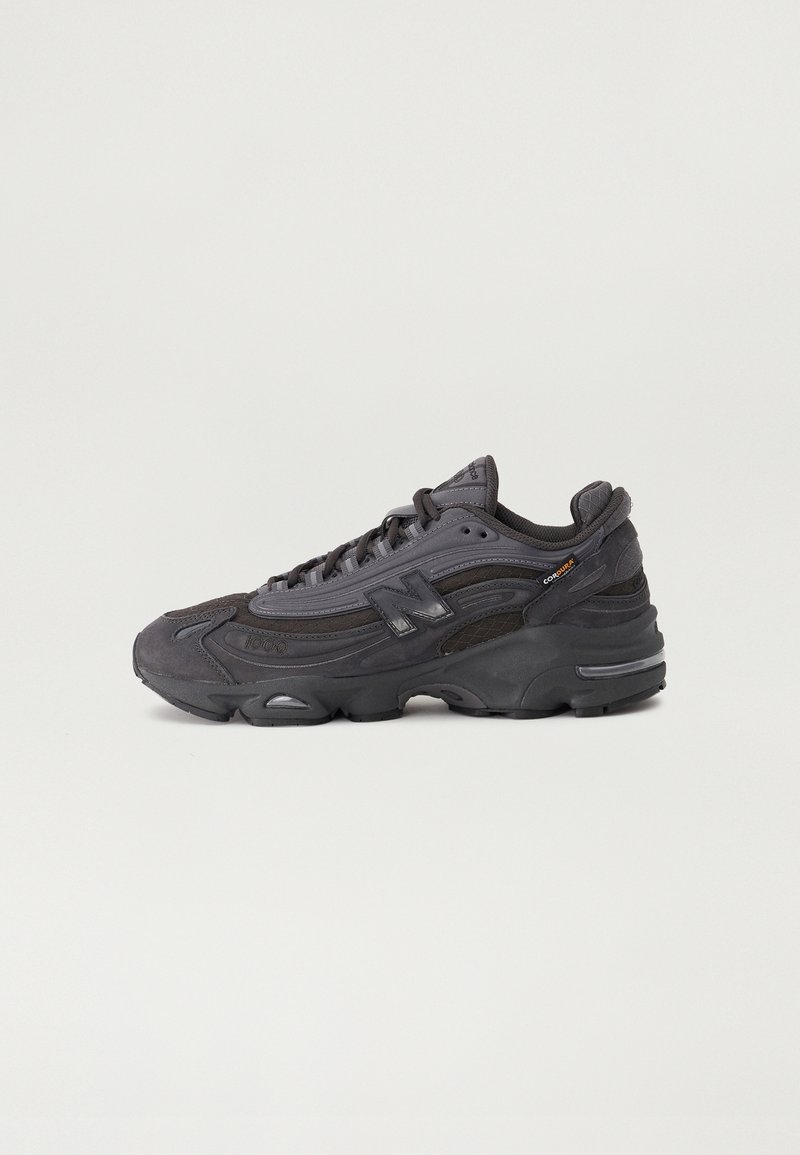 Baskets de sport New Balance noires et gris foncé avec des détails en mesh et en suède, semelle épaisse et logo de la marque sur le côté.