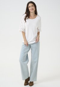 Hvid top med blonder korte ærmer, parret med lyseblå wide-leg jeans og brune ankelstøvler. Simpelt design med en afslappet pasform.
