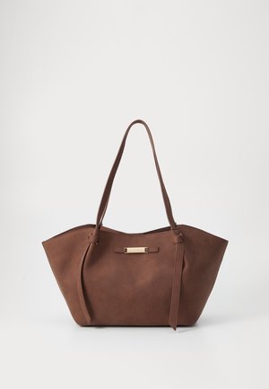 Brązowa torba typu tote ze skóry, z dwoma paskami na ramię i małą poziomą metalową plakietką z logo na środku przodu.