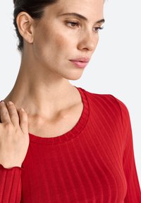 Rød ribbet langærmet top med rund halsudskæring. Stoffet ser glat ud med en let glans, prydet med subtile lodrette linjer og tætsiddende ærmer.
