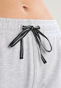 Pantalones jogger de algodón gris con cintura ajustable mediante cordón. El cordón presenta rayas en blanco y negro, y ojales de metal. Textura suave, diseño casual.