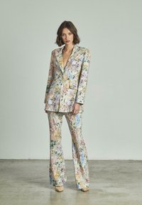 Completo giacca floreale e pantaloni a zampa. Caratterizzato da colori pastello, intricati motivi floreali e un design a un bottone con tasche applicate.