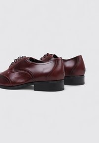 Zapatos de cuero burdeos con una textura suave, puntera redonda y tacón bajo negro. Presentan cordones y sutilezas en los detalles de costura.