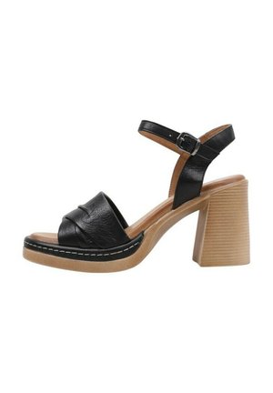 Sandalias de tacón de cuero negro con una correa ancha, que presentan un diseño anudado y un tacón de bloque de madera gruesa con textura en relieve.