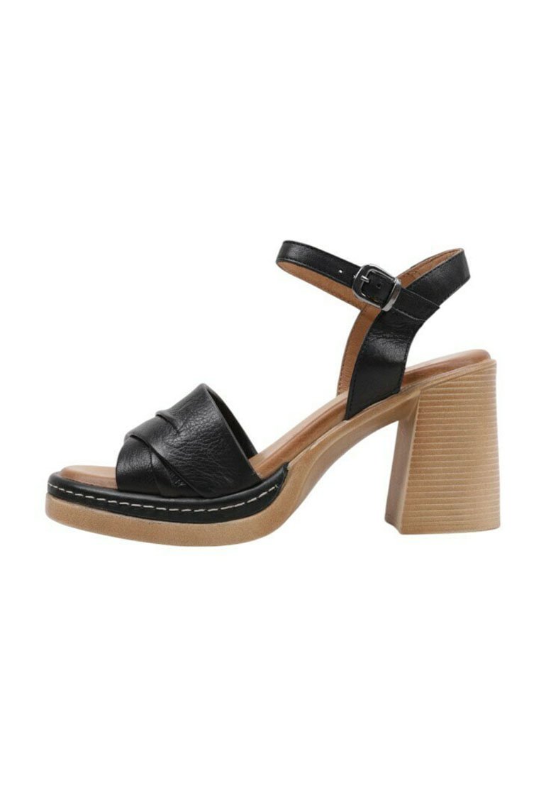Sandalias de tacón de cuero negro con una correa ancha, que presentan un diseño anudado y un tacón de bloque de madera gruesa con textura en relieve.