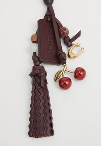 Porte-clés en cuir bourgogne avec texture zigzag, charm en forme de cerise doré et perles en résine mélangées. Comprend une étiquette de marque pour l'identification.