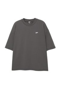 Grå oversized T-shirt med korte ærmer, rund hals og hvidt logo på venstre bryst. Fremstillet af blødt bomuldsstof.