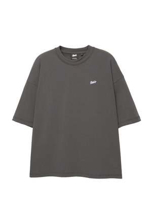Graues, übergroßes T-Shirt mit kurzen Ärmeln, Rundhalsausschnitt und weißen Logodetails auf der oberen linken Brust. Hergestellt aus weichem Baumwollstoff.