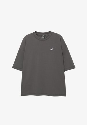 Grå oversized T-shirt med korte ærmer, rund hals og hvidt logo på venstre bryst. Fremstillet af blødt bomuldsstof.