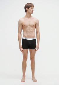 Cuecas boxer pretas com uma cintura elástica branca com o logótipo "POLO RALPH LAUREN", exibidas num modelo masculino com físico atlético.