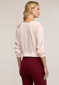 Blusa cropped rosa chiaro con una texture liscia, maniche a sbuffo e una vita attillata, abbinata a pantaloni bordeaux aderenti.