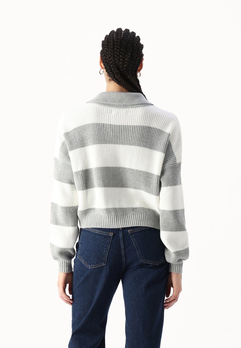 Przycięty sweter w szare i białe paski, z prążkowaną teksturą, szerokim kołnierzem i luźnym krojem, zestawiony z niebieskimi dżinsami o wysokim stanie.