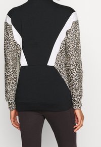 Zwarte sweatshirt met mouwen in panterprint, witte accenten en een gestructureerde afwerking. Het ontwerp bevat contrasterende geometrische vormen en ribbels aan de onderzijde.