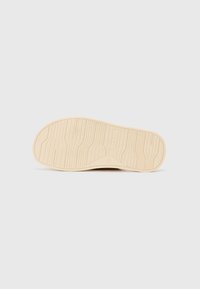 Semelle de chaussure en caoutchouc beige avec motifs de surface texturés, présentant un logo et des rainures pour la traction, avec une base de couleur crème.